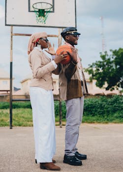 Two stylish friends enjoy a sunny outdoor basketball game, showcasing unique fashion.
