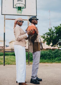 Stylish adults with basketball on outdoor court, showcasing modern fashion.