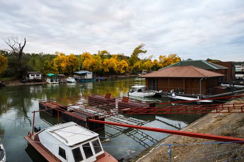 Free Tranquil river scene featuring boats and autumn foliage near wooden cabins. Stock Photo
