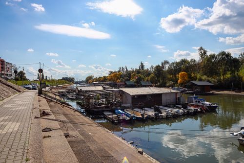 Free Picturesque riverside scene with boats and sidewalk under a vibrant fall sky. Stock Photo