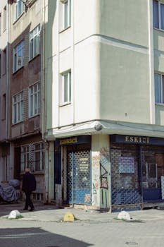 A closed shop with graffiti on a sunny city street corner, casting shadows of a walking person.