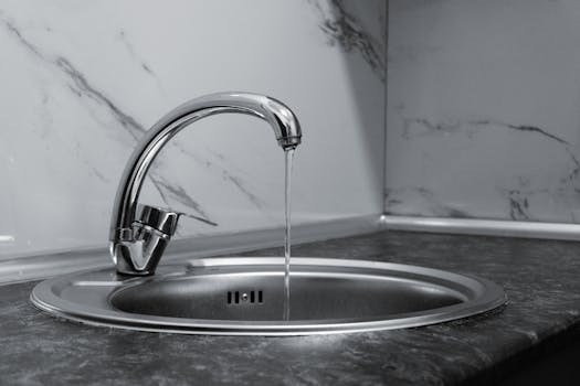 Chrome faucet with running water in a modern kitchen with marble countertop.