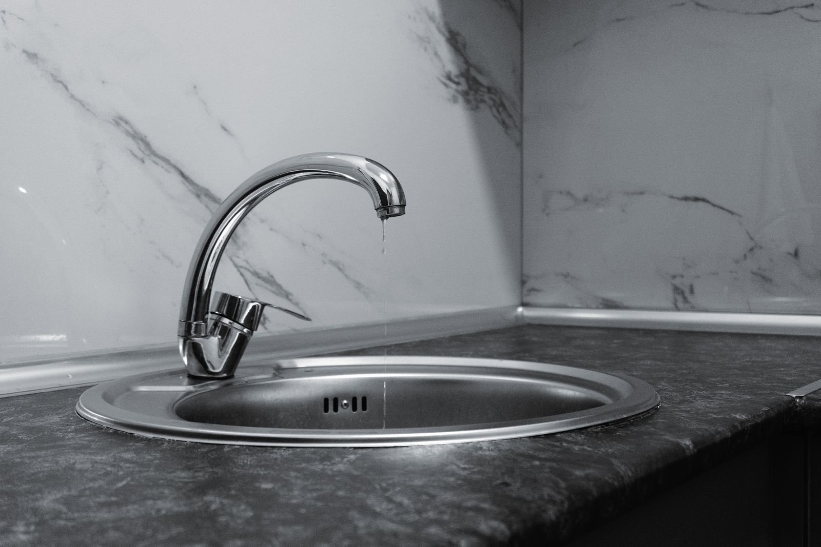Close-up of a dripping kitchen tap above a clean sink basin