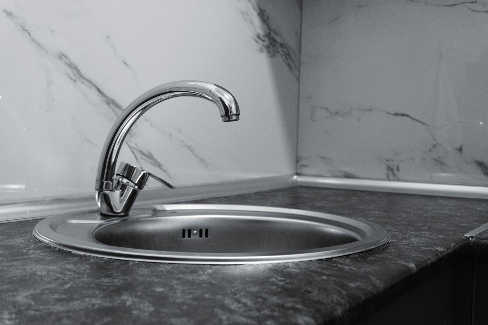 Stainless steel kitchen sink and faucet set against a marble backsplash