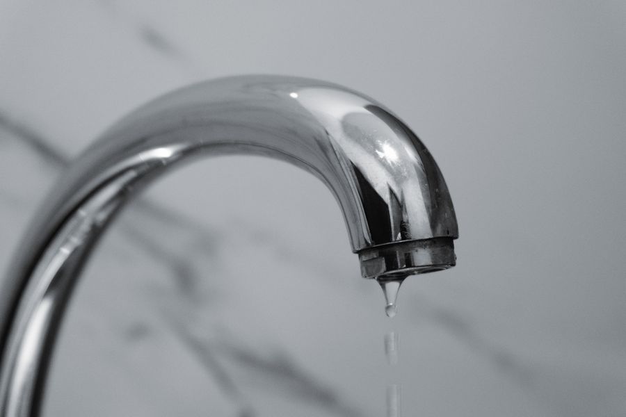 Close-up of a chrome bathroom faucet with a drop of water falling from it
