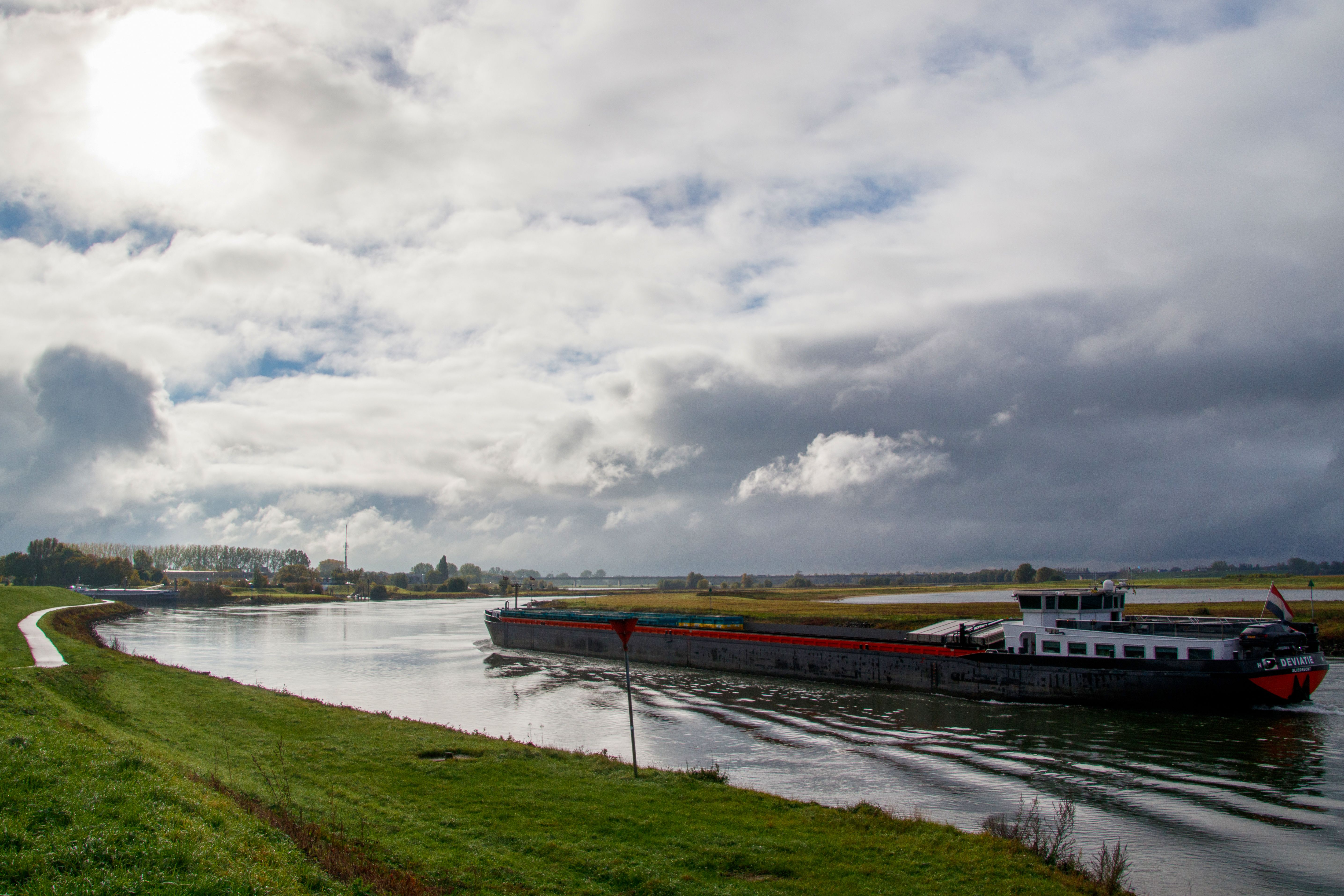 A cargo barge navigates a river under a cloudy sky, offering a serene riverine scene.