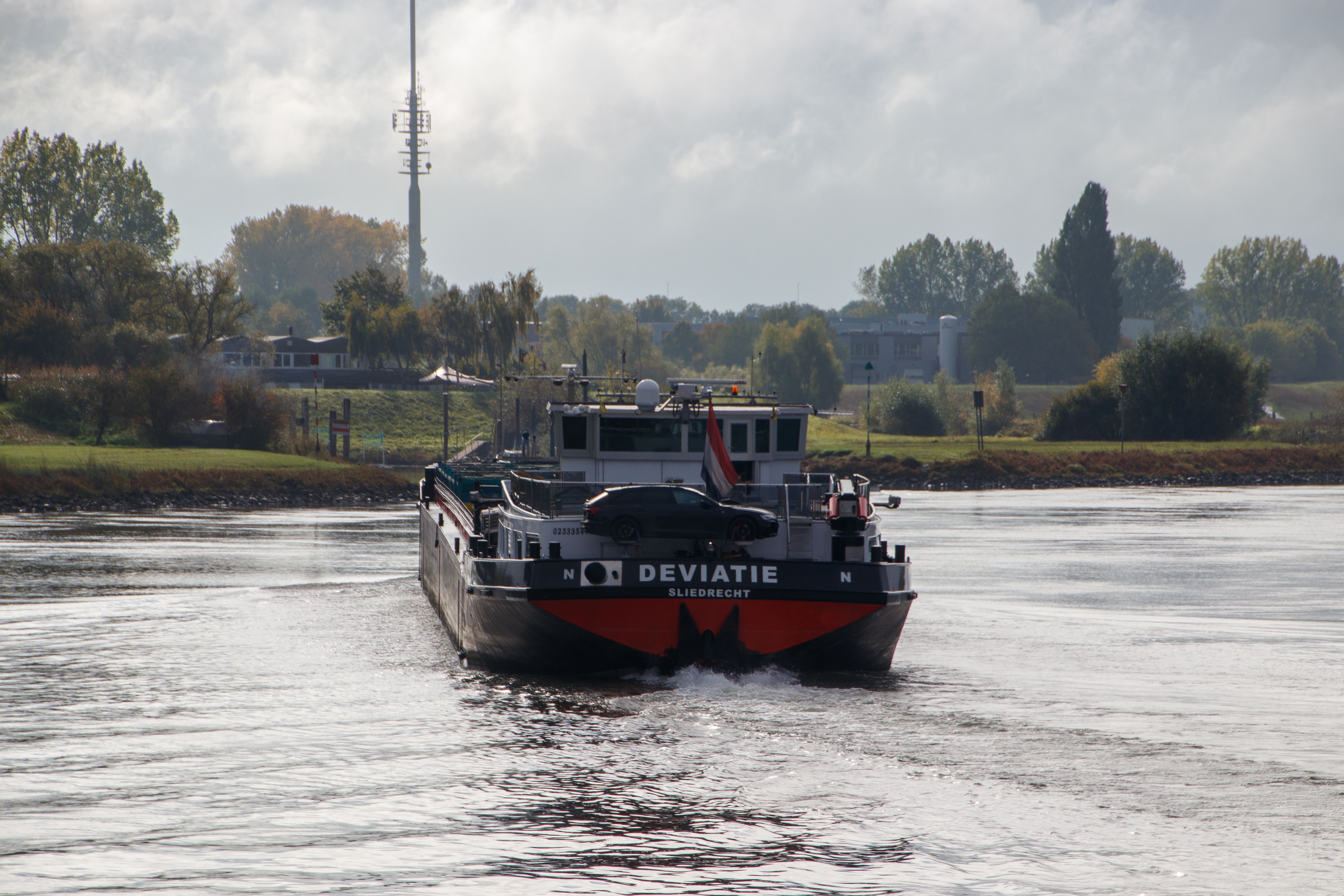 A cargo ship named Dev atie on a river with a scenic background, navigating through calm waters.