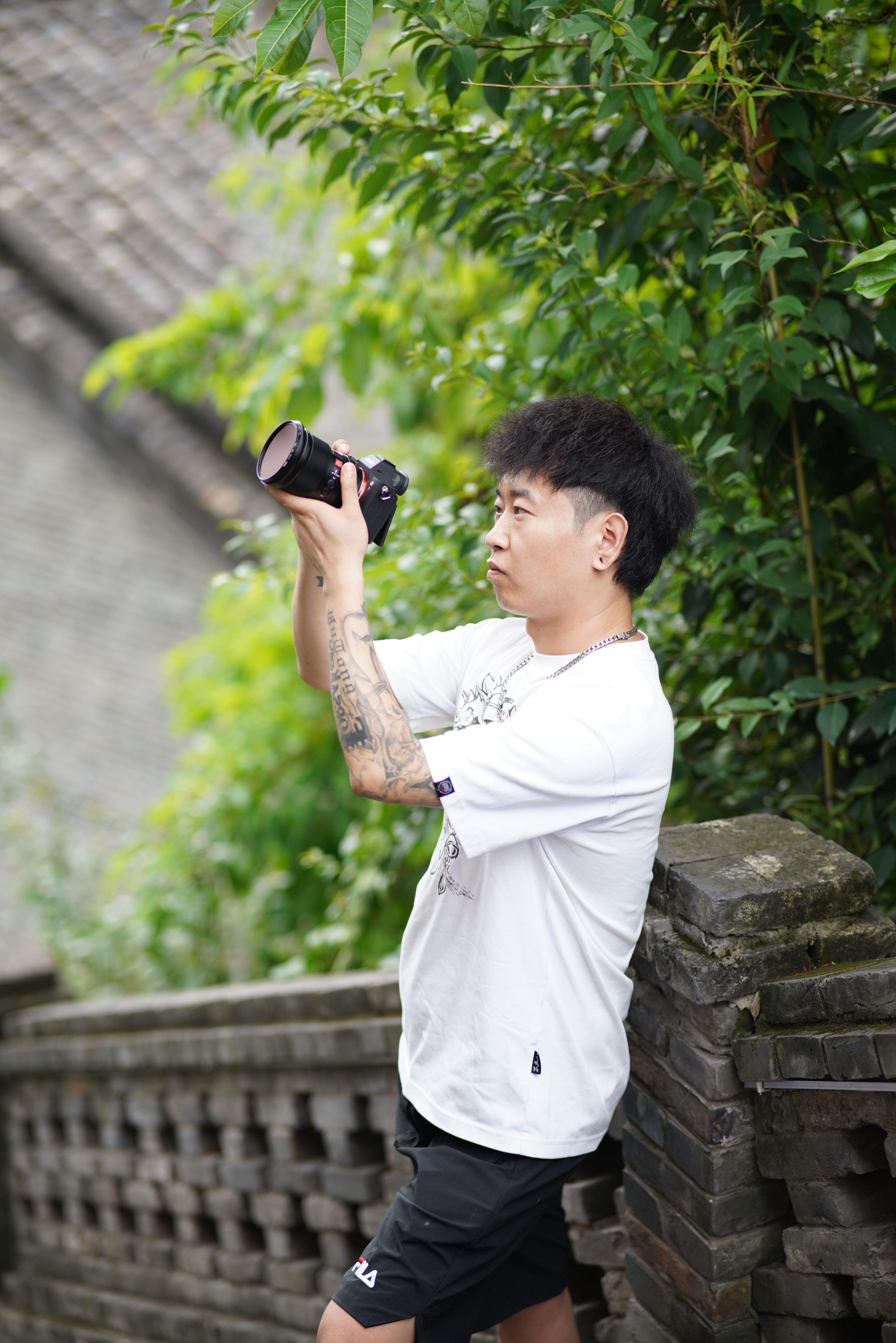 Photographer in action leaning on a stone railing, capturing photos in a lush urban setting.