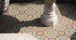 Intricate Moroccan tiles and marble column in natural light, showcasing vibrant patterns.
