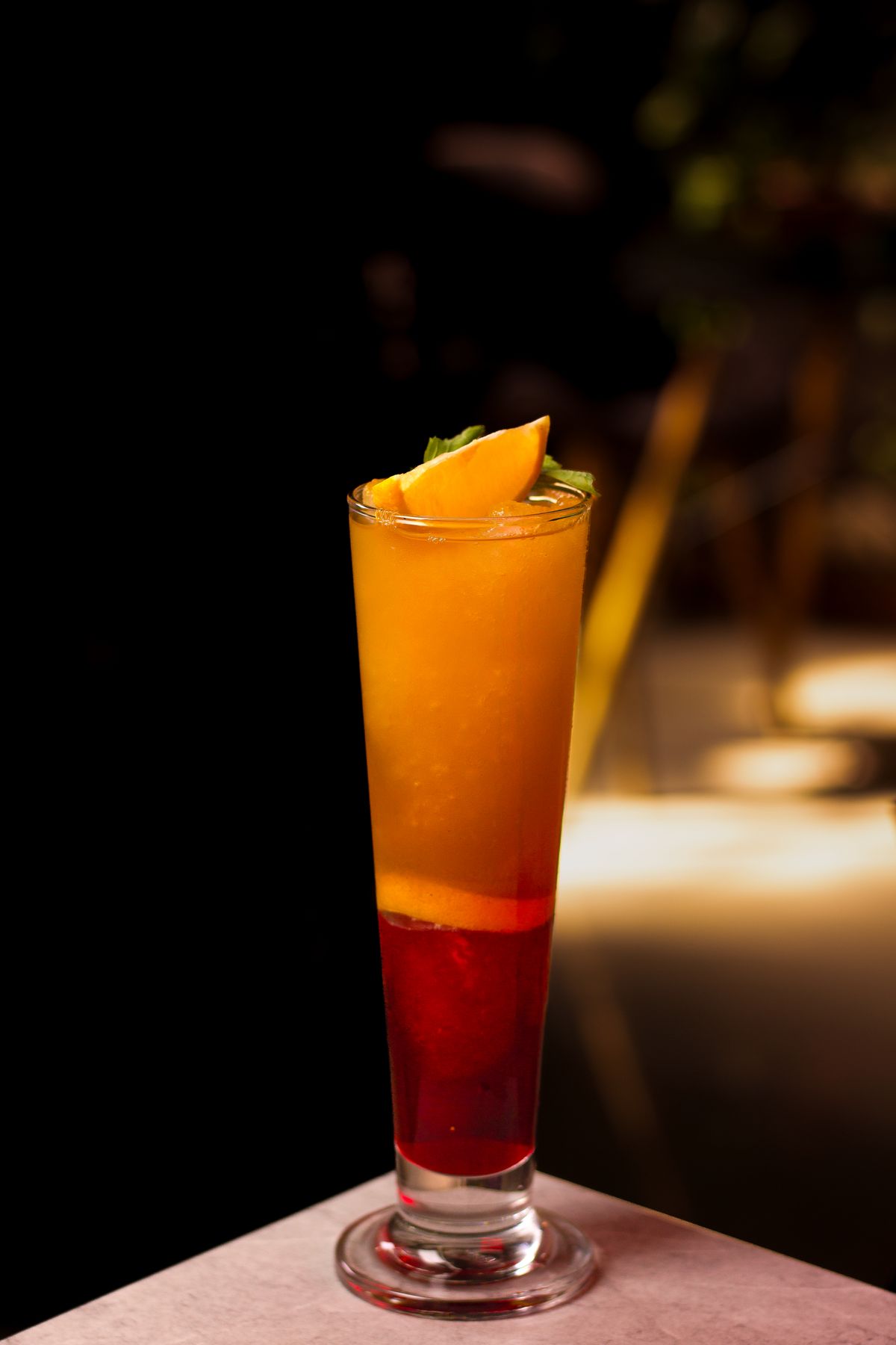Gelaagd rood en oranje drankje met een schijf citrus