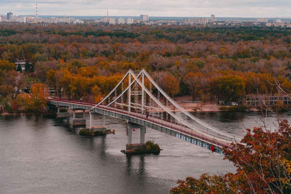 A scenic view of the pedestrian bridge over the Dnieper River with autumn foliage in Kyiv, Ukraine.