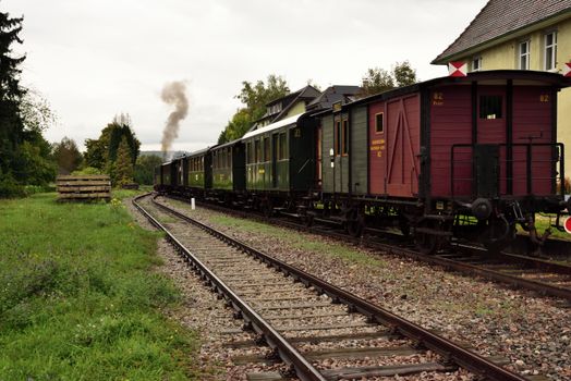 A vintage steam train travels through Kandern, Germany, showcasing historic railway charm in an autumn setting., free online jigsaw puzzle on JigsawPuzzlesFreeOnline.org