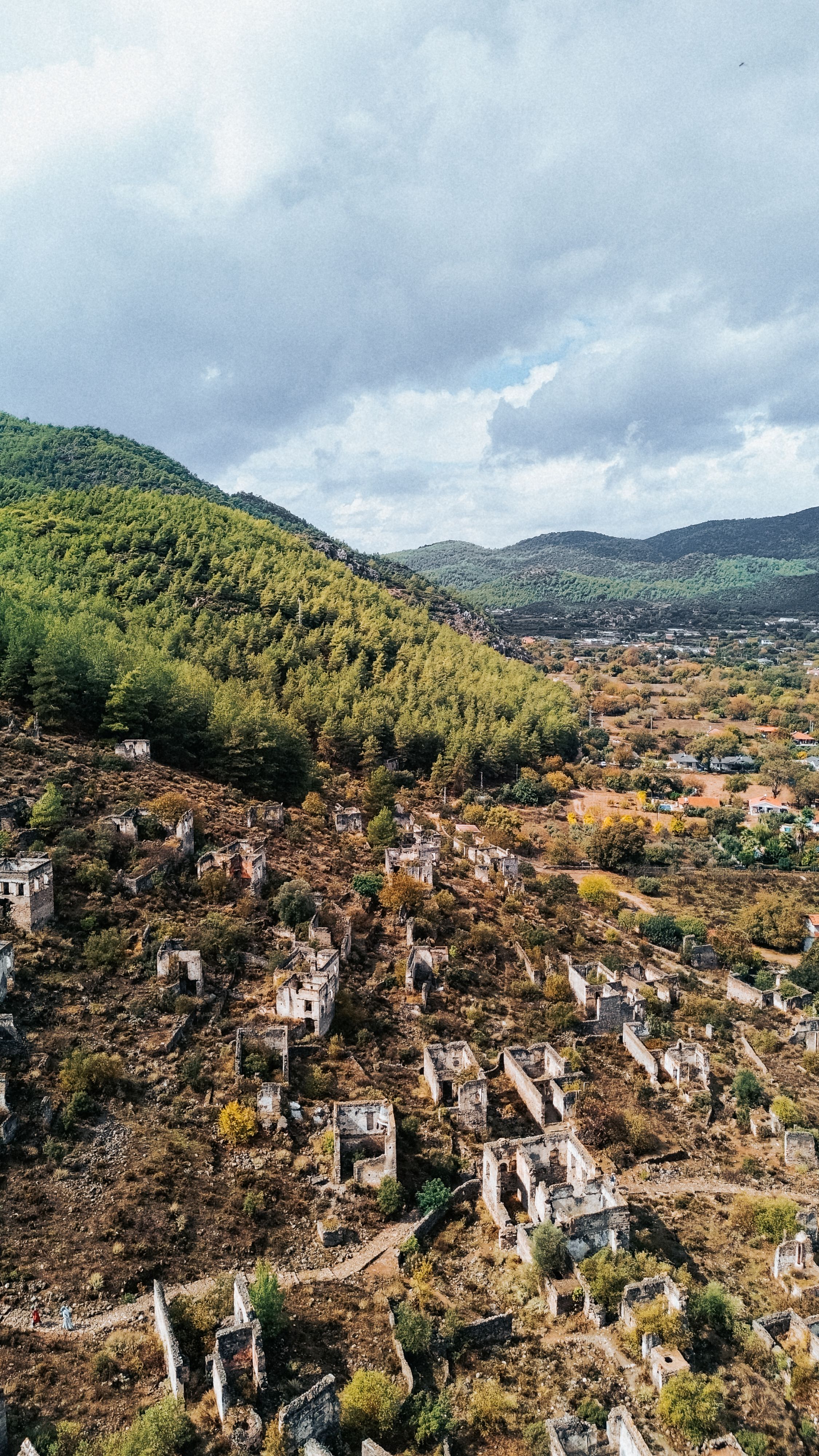Drone shot capturing the historical ruins of the abandoned village of Kayaköy in Turkey, surrounded by lush greenery.
