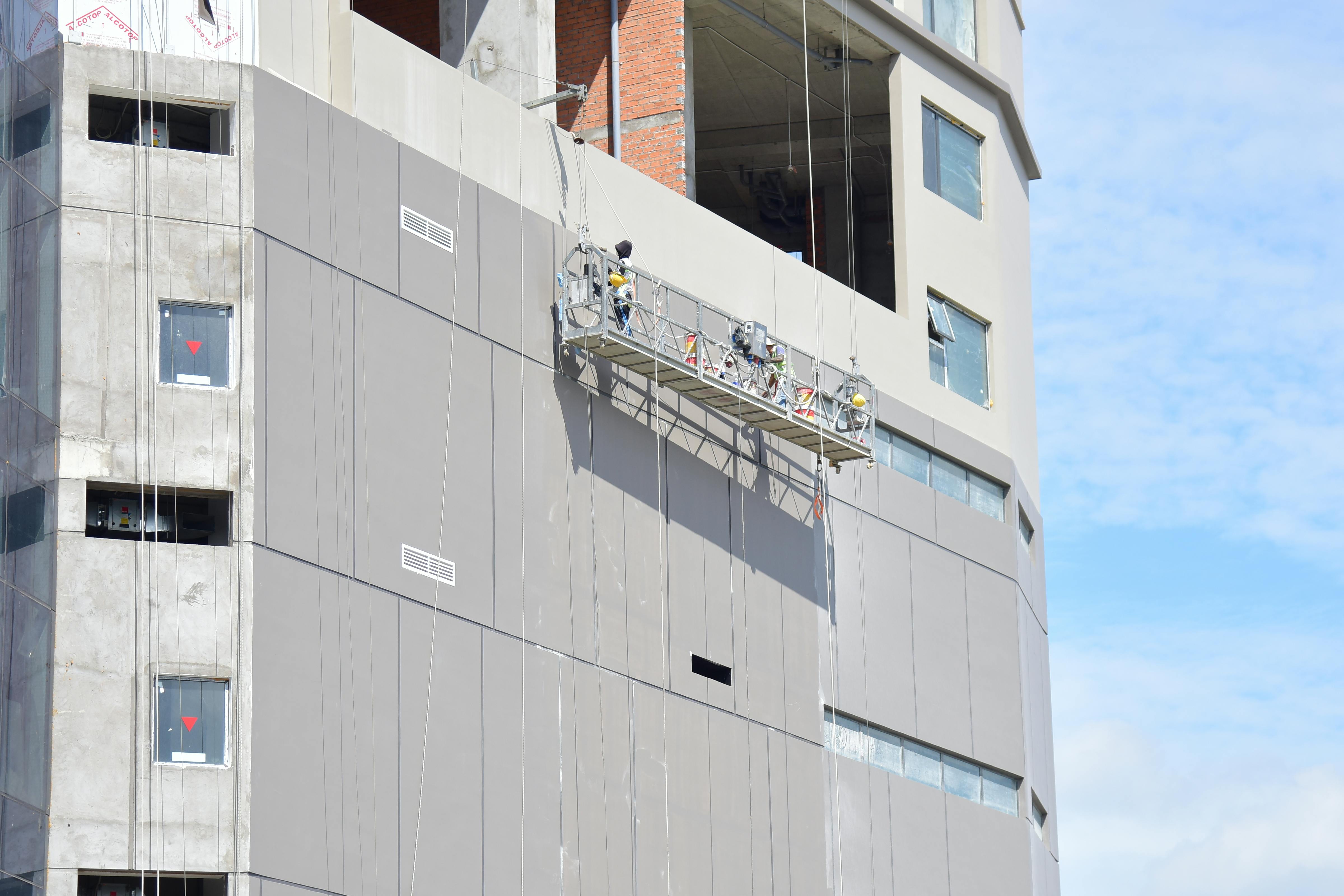 Workers on a suspended platform conducting maintenance on a high-rise building facade.
