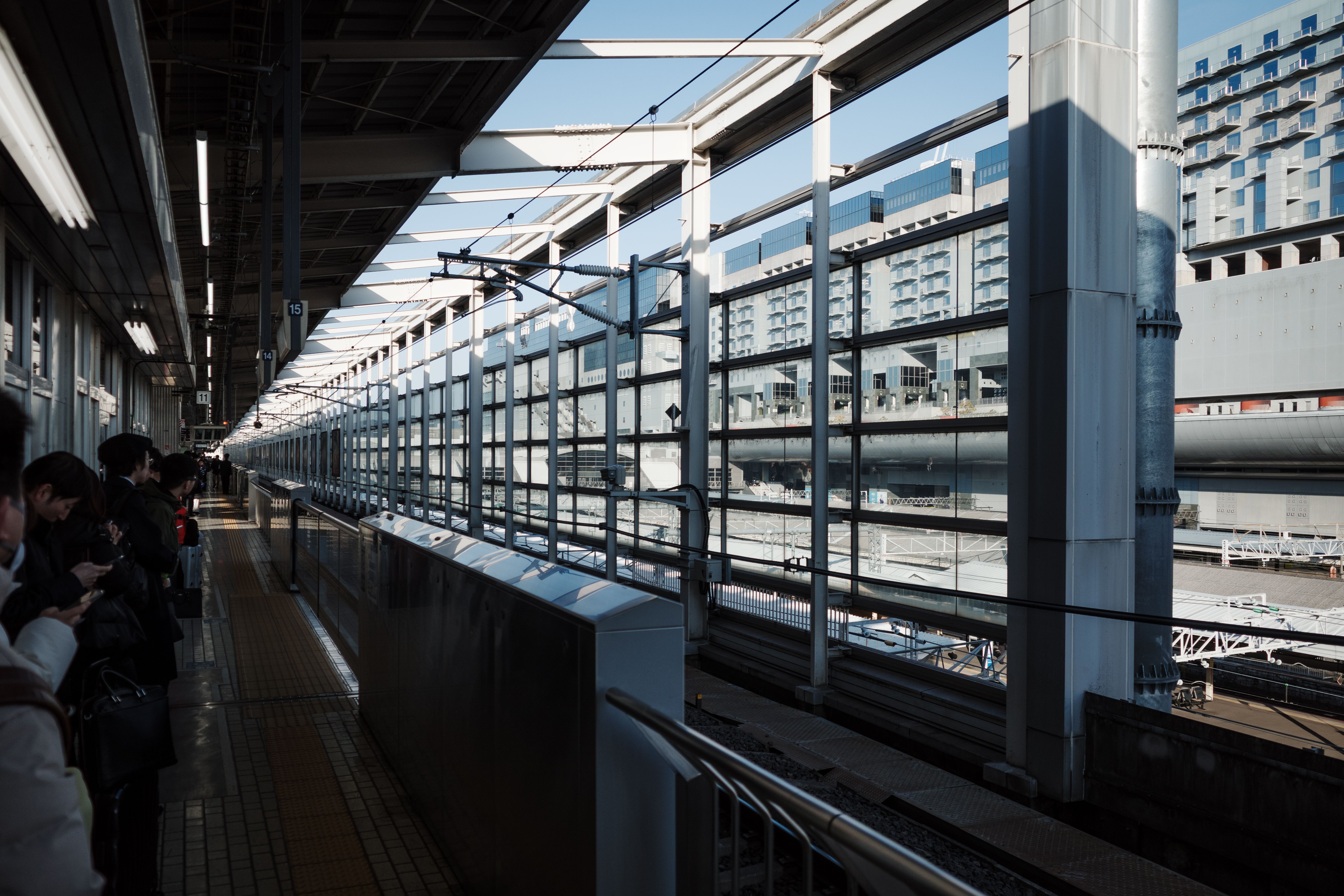 Passengers waiting on a sunny platform at Kyoto Station under a steel roof