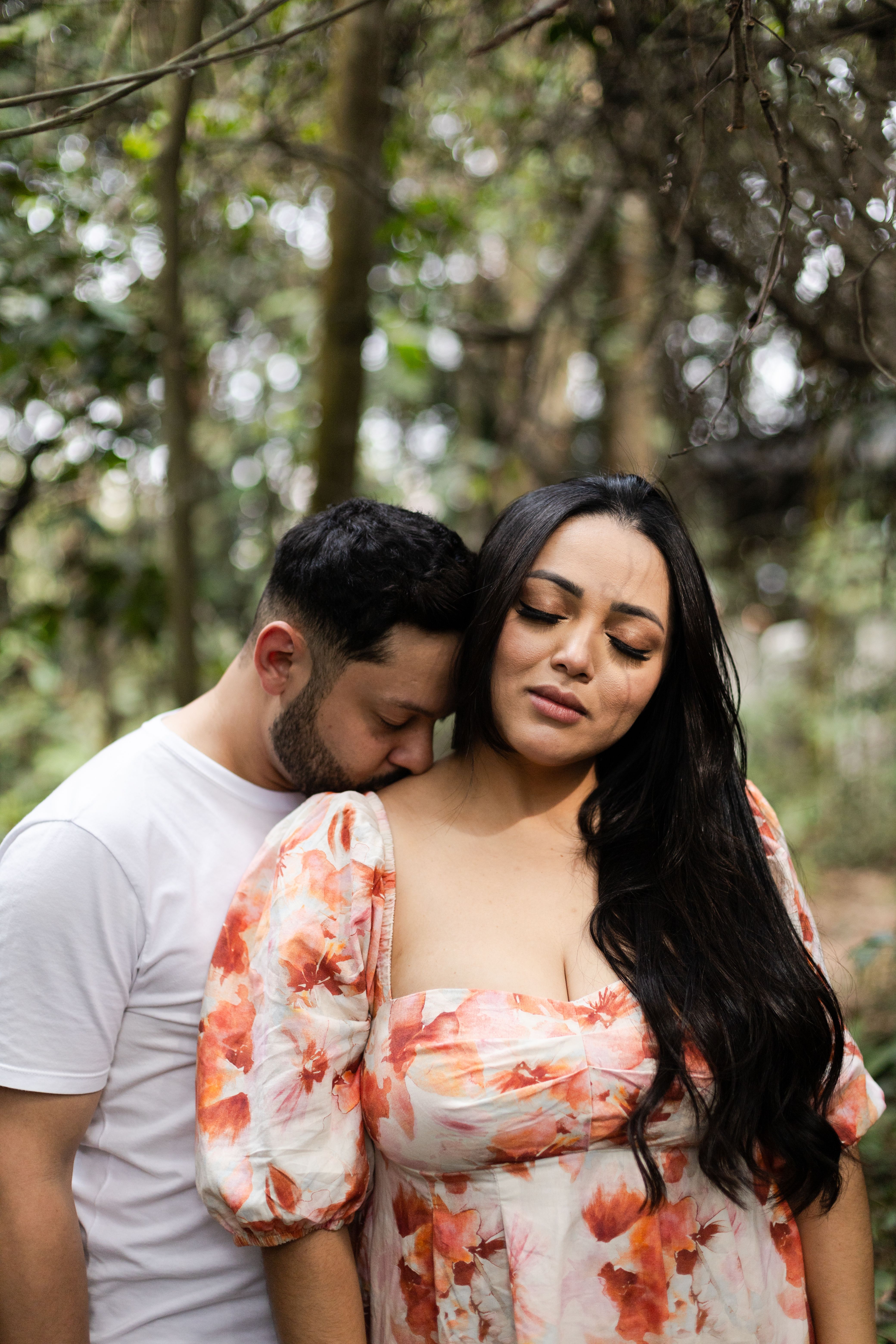 A loving couple shares an intimate moment in a lush São Paulo forest, creating a warm, romantic scene.