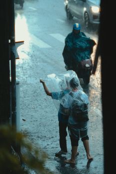 Two individuals using plastic covers for rain protection on a city street.