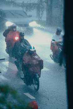 Group of motorcyclists braving heavy rain on a city street, wearing ponchos for protection.