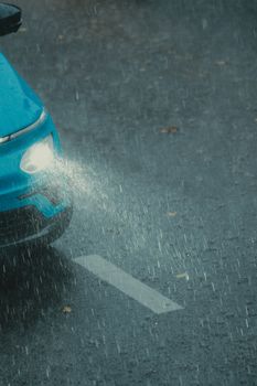 Blue car navigating a rainstorm with headlights on, highlighting a waterlogged road.