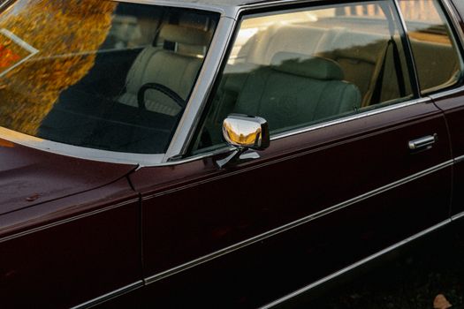 Vintage car with burgundy exterior reflecting warm sunset tones, showcasing retro design details.