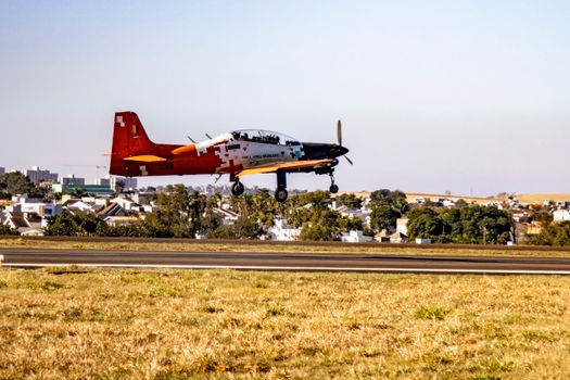 A military airplane captures a landing at an open airfield in Londrina, Brazil under clear skies.