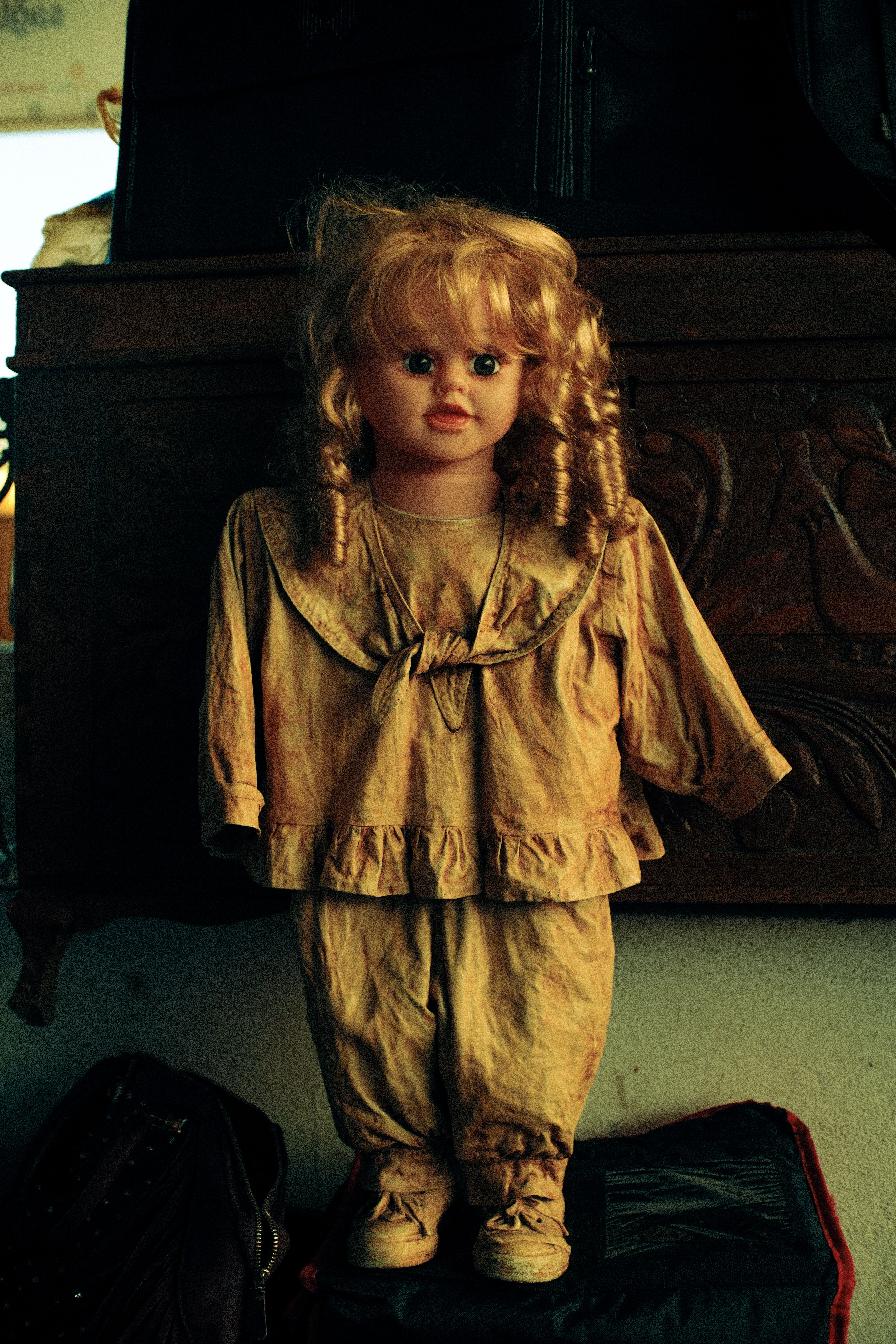 A vintage porcelain doll with curly hair in a rustic, dimly lit environment.