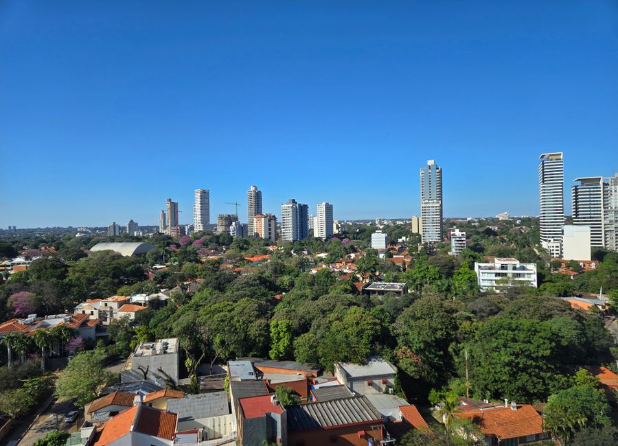 A serene cityscape showcasing a vibrant mix of tall buildings and abundant green spaces under a clear blue sky.