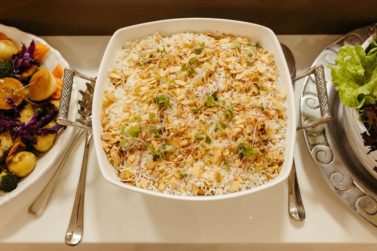 White serving dish of long-grain rice topped with toasted sliced almonds and microgreens