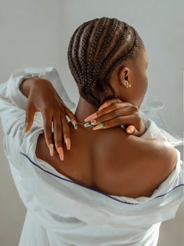 Back view of a stylish black woman with braids and colorful manicure, wearing an off-shoulder shirt.