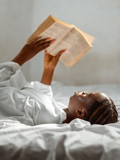 Free A woman lies comfortably on a bed, absorbed in reading a book, conveying peaceful solitude. Stock Photo