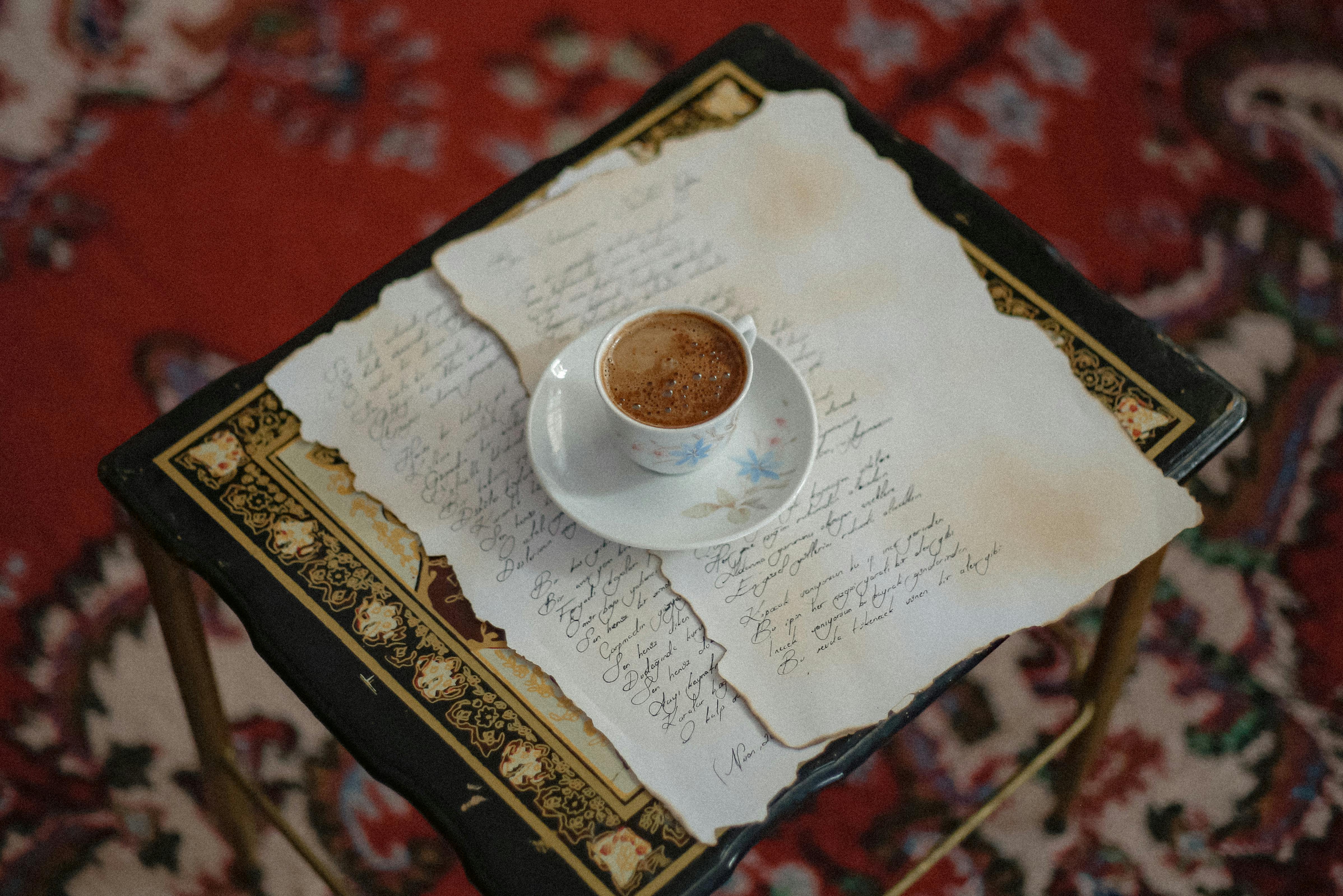 A delicate coffee cup on handwritten letters atop an ornate table with a vintage style, evoking a classic and artistic mood.