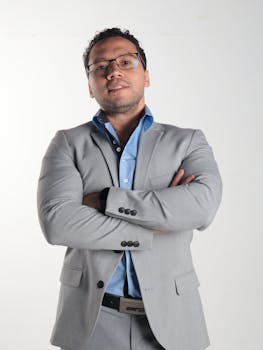 Portrait of a confident man in a gray suit with crossed arms against a white background.