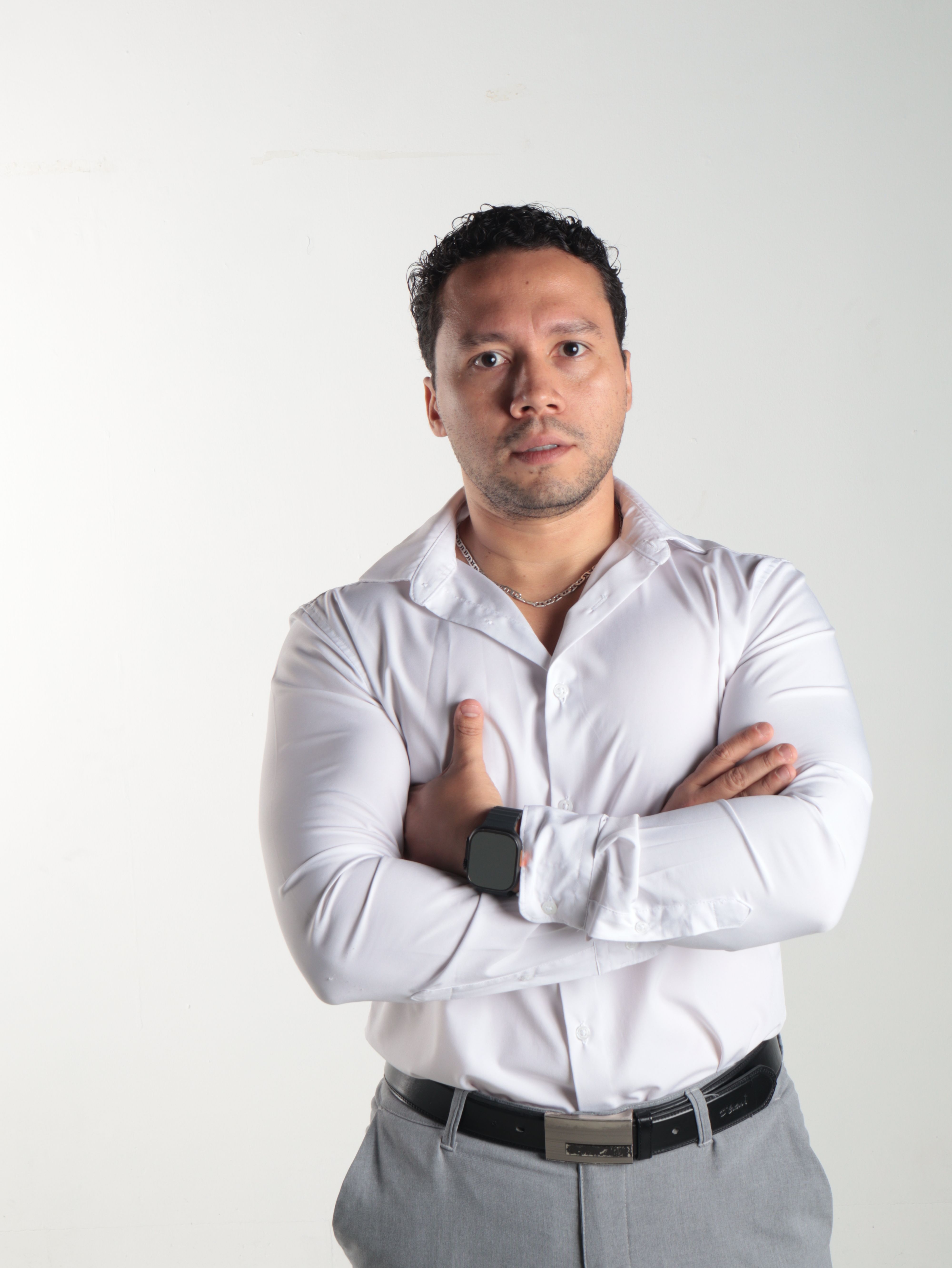 Portrait of a confident man in a crisp white shirt and grey trousers against a plain background.