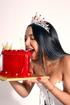 A cheerful woman in a tiara enjoying a festive red cake adorned with a crown.