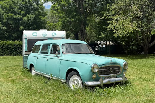 Charming vintage Peugeot and caravan parked in a lush, summer landscape in Saint-Lary-Soulan, France.