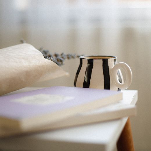 Striped bell-shaped mug on a stack of books — photo by betül nur akyürek on Pexels