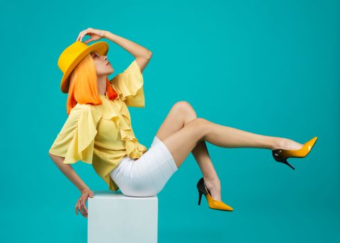 Stylish woman in vibrant yellow and white fashion in a modern pose on a blue background.