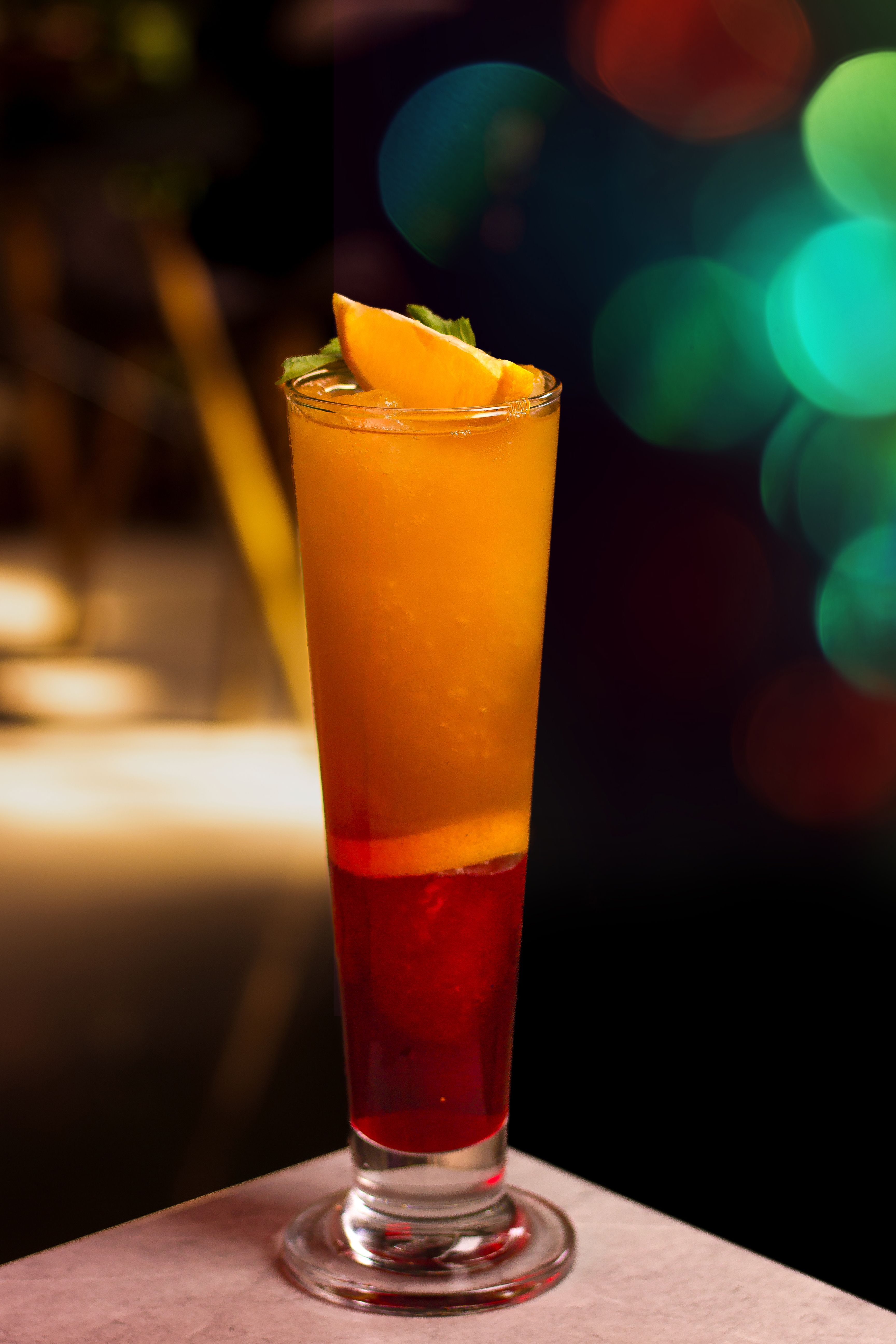 A tall glass of tequila sunrise showing the orange juice on top and a deep red grenadine layer settling at the bottom, garnished with an orange slice and cherry.