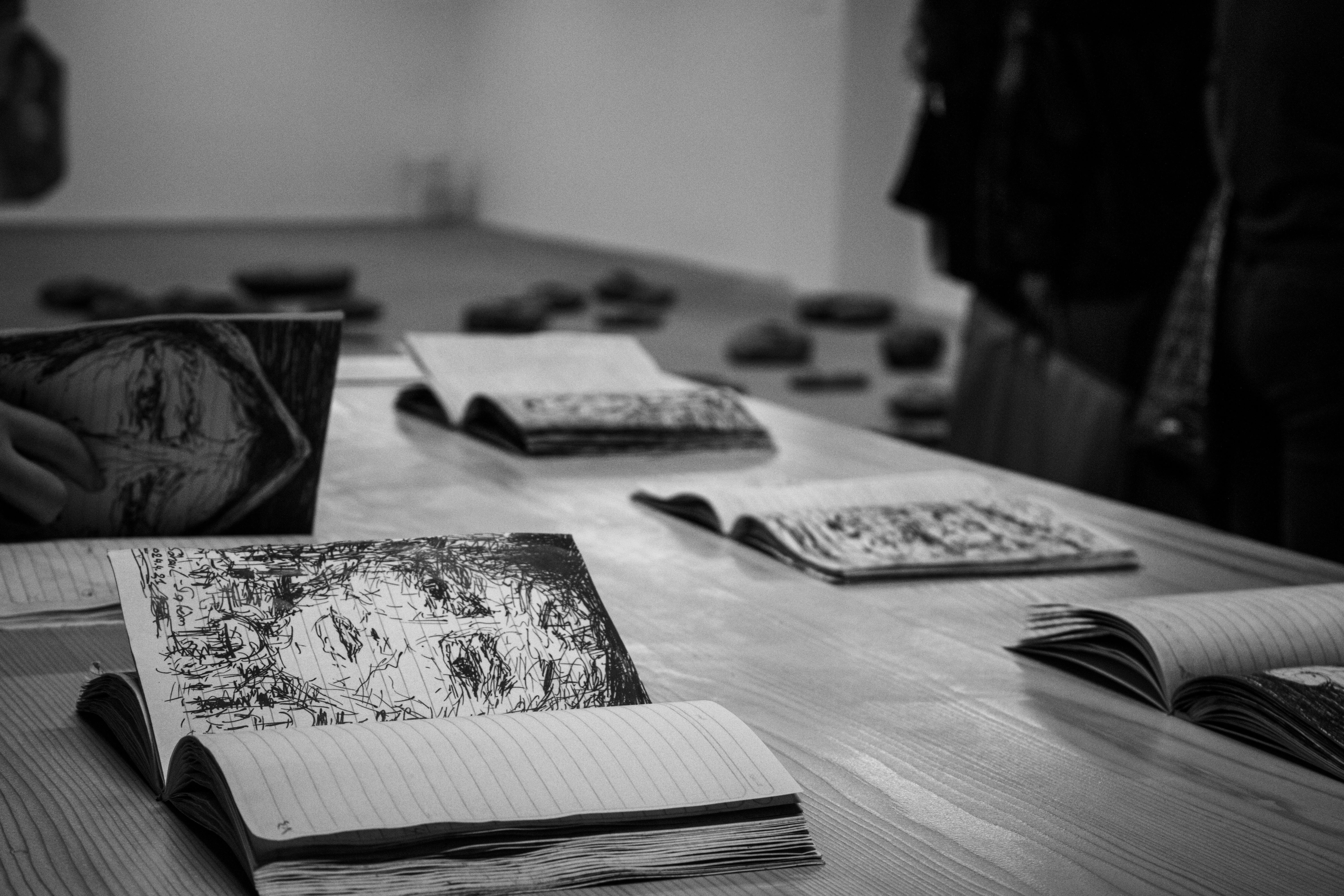 Sketchbooks laid open on a gallery table, the quiet labour behind finished work