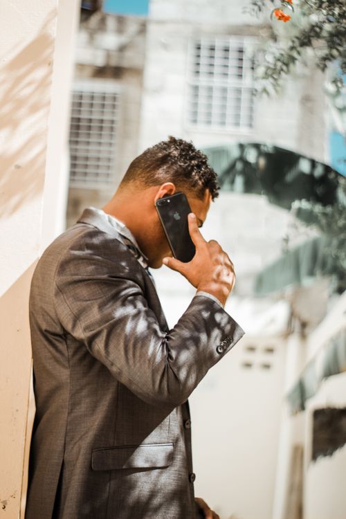 Free Young businessman in a gray suit talking on a phone in a sunny urban setting. Stock Photo