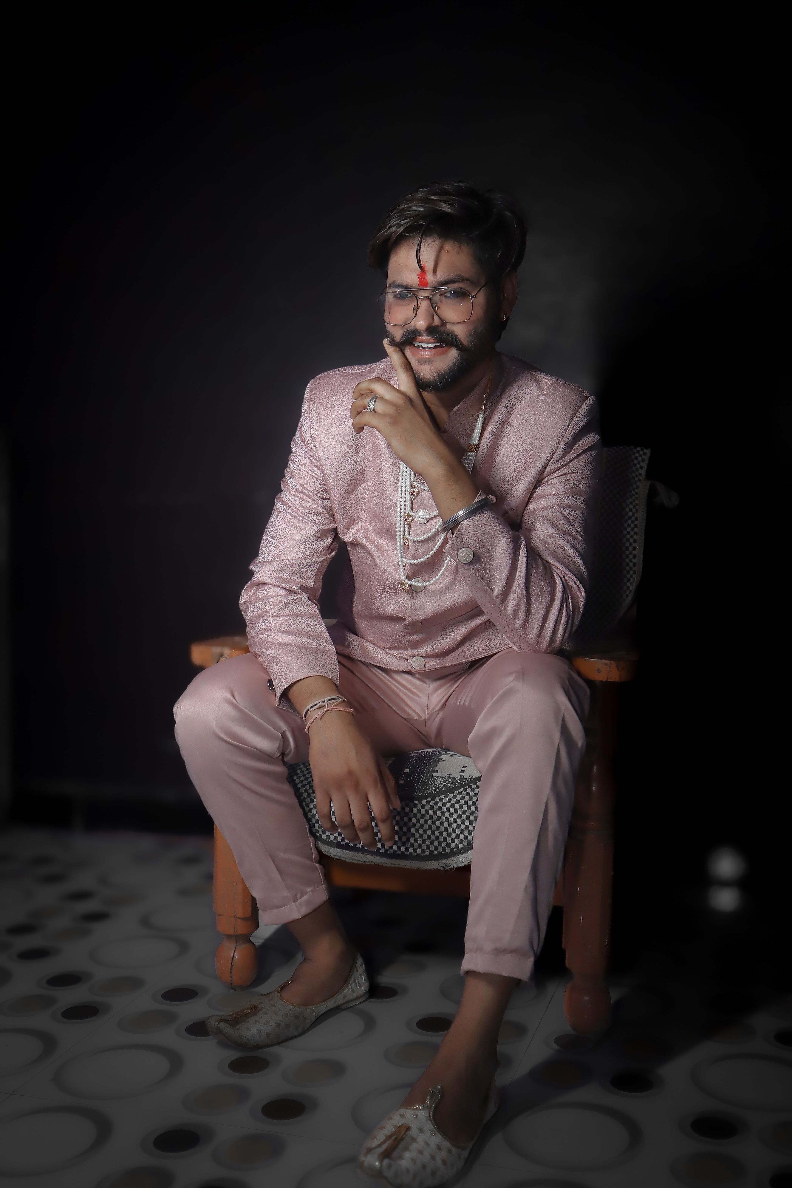 A man in traditional attire, seated indoors with a confident smile, exuding elegance.