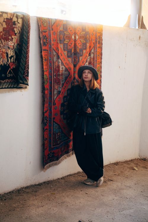 Free Woman in fashionable attire poses beside vibrant rug in Antalya market. Stock Photo