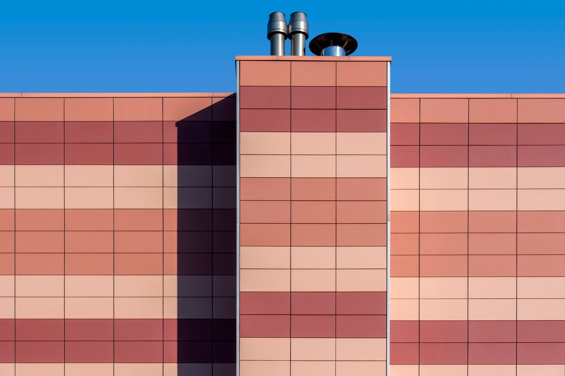 Orange and red tiled industrial facade with geometric pattern under a clear blue sky.