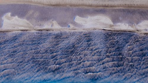 Free Stunning aerial capture of rippled waves meeting the shore under soft dawn light, showcasing nature's beauty. Stock Photo