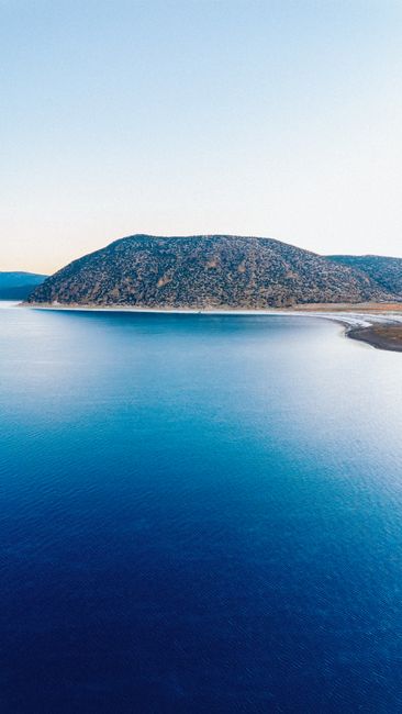 Breathtaking aerial view of a tranquil lake meeting a mountainous landscape under a clear blue sky.