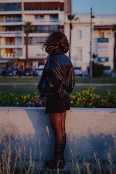 Woman in stylish outfit stands against urban backdrop at sunset, adding a modern touch.