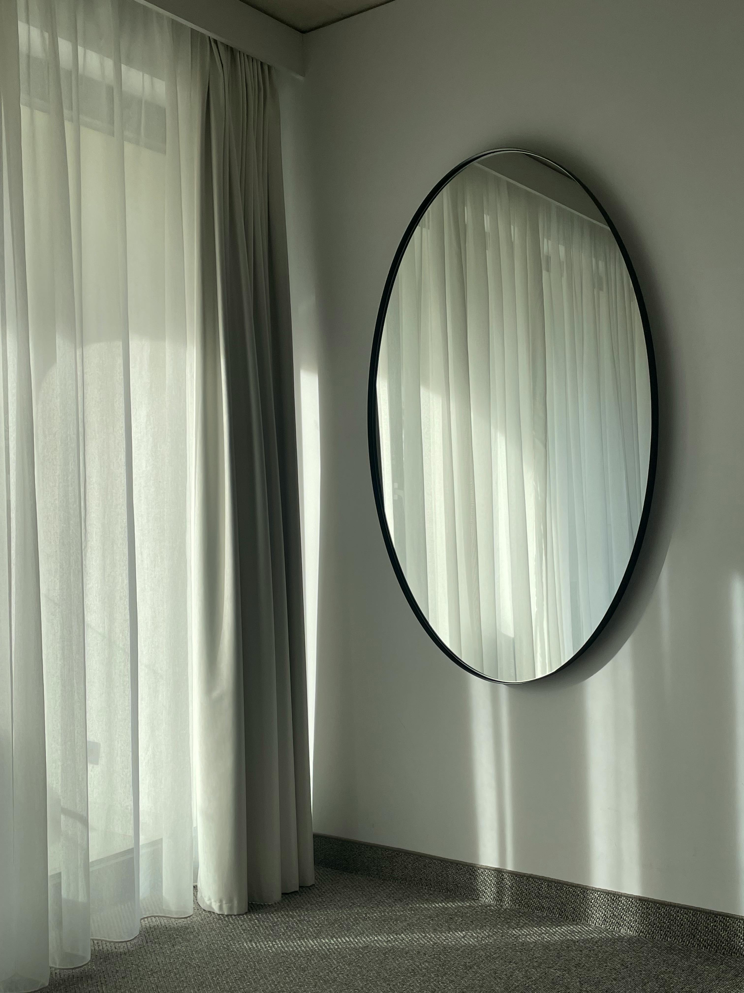 A serene minimalist room featuring a round wall mirror and sheer curtains.