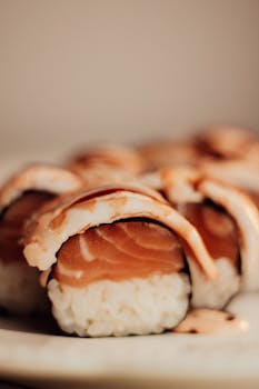 Appetizing close-up of salmon sushi rolls topped with creamy sauce on a plate.