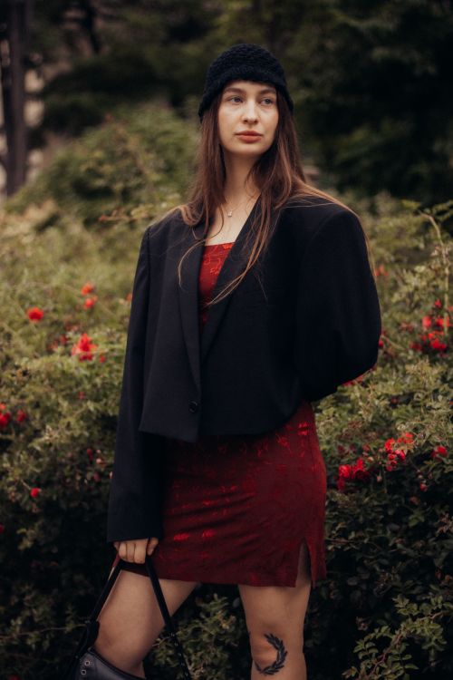 Free Woman in red dress with black coat standing in garden, exuding elegance. Stock Photo
