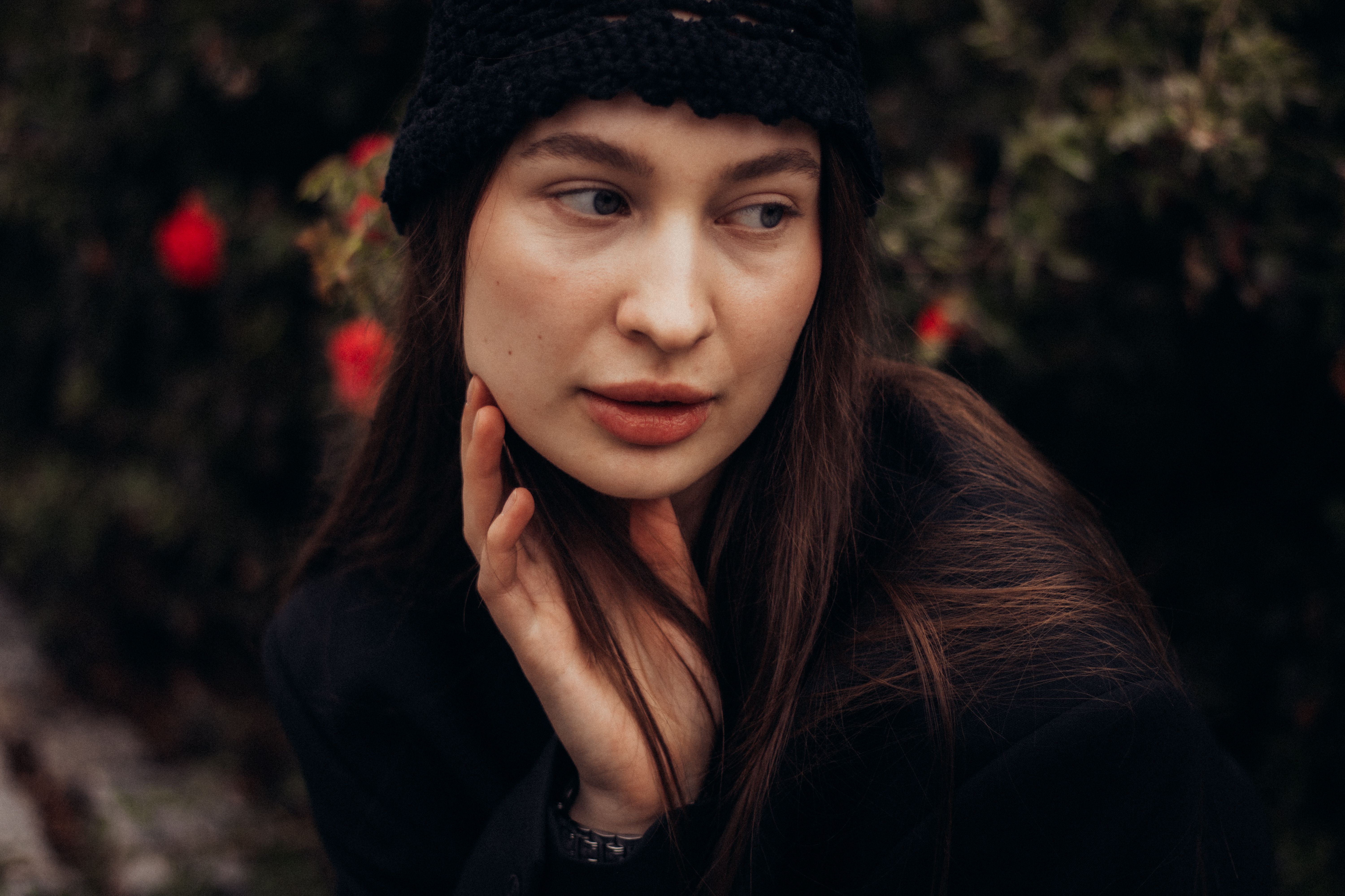A woman wearing a black hat looks thoughtfully to the side, surrounded by nature\'s beauty.